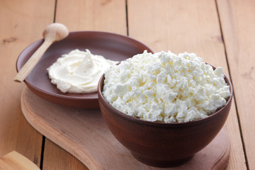 Cheese, cottage cheese and cream in clay ware, fresh curd on a wooden background, rustic sour cream, brown shade, healthy food, French breakfast, top view, goat curd, protein