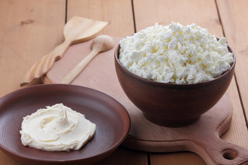 Cheese, cottage cheese and cream in clay ware, fresh curd on a wooden background, rustic sour cream, brown shade, healthy food, French breakfast, top view, goat curd, protein