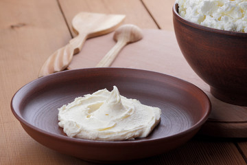 Cheese, cottage cheese and cream in clay ware, fresh curd on a wooden background, rustic sour cream, brown shade, healthy food, French breakfast, top view, goat curd, protein