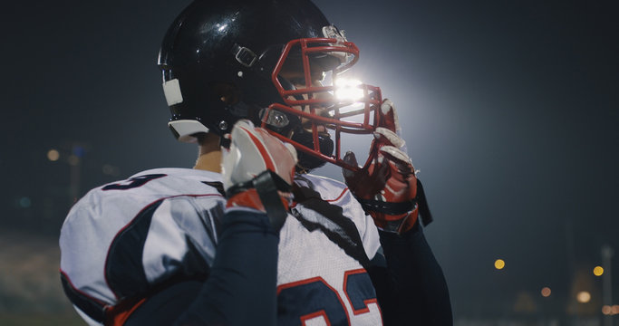 American Football Player Putting On Helmet on large stadium with lights in background