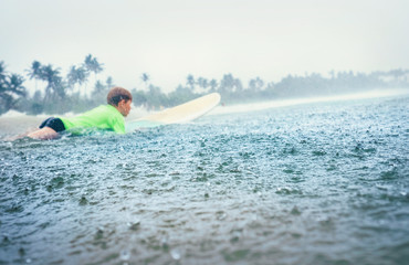 Boy first step surfer learning to surf under tropical rain