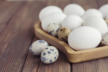 Obraz premium White eggs and quail eggs in wooden heart shaped plate on wooden brown background