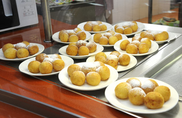 Donuts with a powdered sugar placed on a canteen counter. 