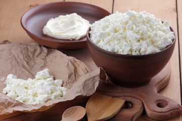 Cheese, cottage cheese and cream in clay pots, fresh cottage cheese on a wooden background, sour cream in rustic style, healthy food, French breakfast, top view, goat curd on parchment paper, protein