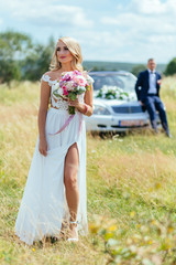 Obraz premium Bride stands on the grass before a car and a groom