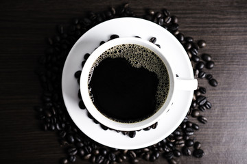 Black coffee in white cup and coffee bean on wood table background.