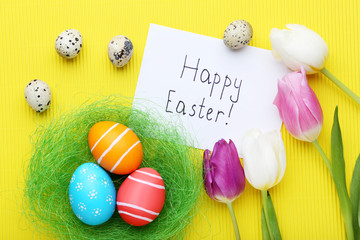 Inscription Happy Easter with painted eggs and tulips on yellow background