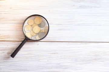 Magnifier on a wooden background with coins. Concept of the financial market