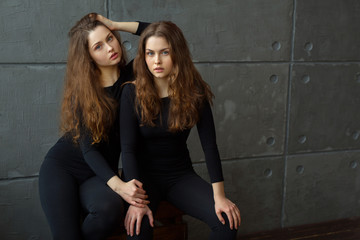 Fototapeta na wymiar portrait of two beautiful young girls of twin sisters with flowing hair against the gray wall in the interior