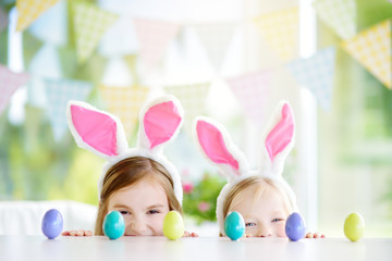 Two cute little sisters wearing bunny ears playing egg hunt on Easter