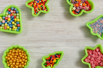 Multicolored sweets in baking molds. Place for text. Sugar confetti for a cake on a white wooden table. View from above.