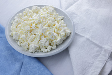 Cheese, cottage cheese on a white plate, fresh cottage cheese on a white and blue napkin, dairy product on a white background, healthy food, French breakfast, top view, goat curd in minimalist style, 