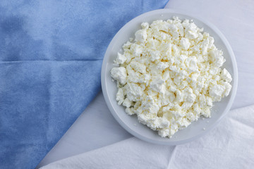 Cheese, cottage cheese on a white plate, fresh cottage cheese on a white and blue napkin, dairy product on a white background, healthy food, French breakfast, top view, goat curd in minimalist style, 