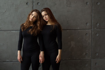 portrait of two beautiful young girls of twin sisters with flowing hair against the gray wall in the interior