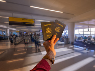 Hand holding two American passports in front of a boarding airline gate