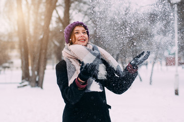 Fototapeta na wymiar Portrait of young beautiful girl in winter. Smiling and enjoying snowfall on warm sunset. Snowy day