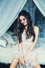 Obraz premium Seductive Woman Fashion Model Sitting on White Vintage Bed