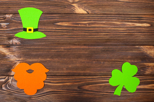 St. Patrick's Day theme colorful horizontal banner. Green leprechaun hat, beard and shamrock leaves on brown wooden background. Felt craft elements. Copy space. For greeting card, banner