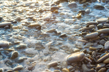 pebble stones on the sea beach, the rolling waves of the sea with foam