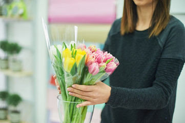 Close-up hands of florist with flowers. Florist holding blooming bouquet of pink tulips on a linen background.