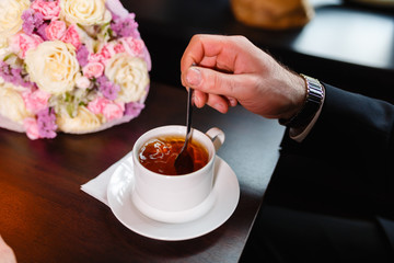 A man in an expensive suit, drinking tea. The businessman interferes with a spoon of tea in a white...