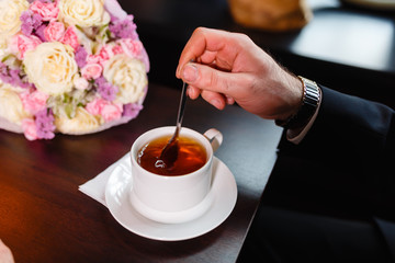 A man in an expensive suit, drinking tea. The businessman interferes with a spoon of tea in a white mug and a white saucer in a close-up cafe.