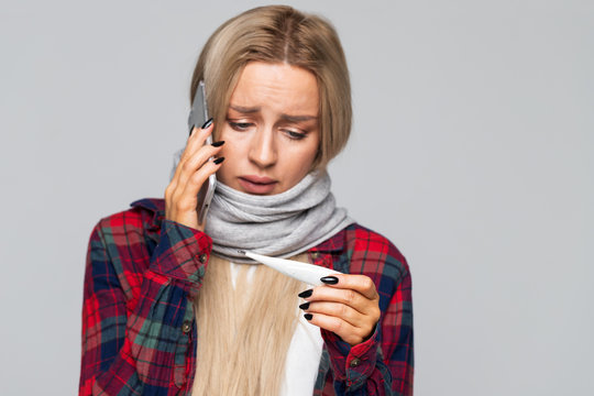 Beautiful Upset Young European Blond Woman In Shirt, Wrapped Scarf Looking At Thermometer And Talking On The Phone/ Sick Desperate Female Has Flu/ Rhinitis, Cold, Sickness, Allergy Concept