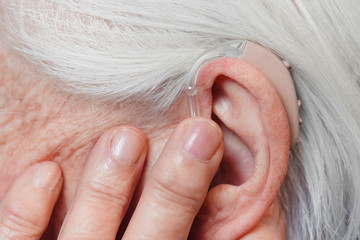 Closeup senior woman with hearing aid in her ear. Health care, hear amplify, device for the deaf.