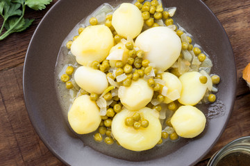 stewed potatoes in green sauce with peas, on wood
