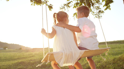 Joung boy and girl swinging on a swing