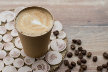 Coffee to go in paper cup on wooden background with coffee beans, place for text