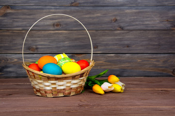 Easter eggs in wicker basket, red and yellow tulips on wooden boards.