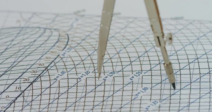 Close up of the steel compass drawing a round on the chart with numbers and formulas. Macro