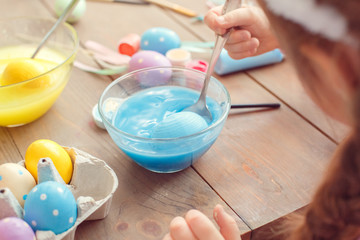 Little cute girl at home easter celebration concept back view close-up coloring eggs dipping egg into blue water