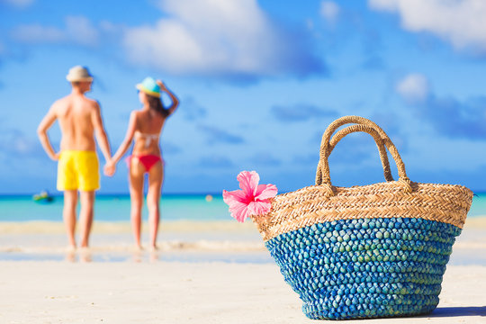 colourful straw beach bag abd hugging honeymoon couple on background