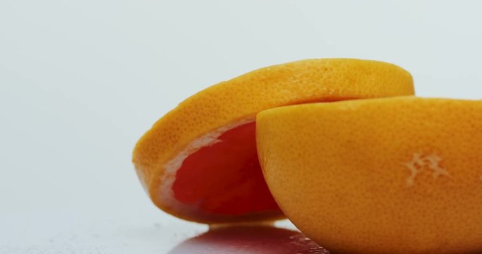Macro of the cutted grapefruit with water drops on rolling in front of the camera on the white background. Close up