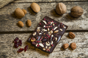 Pieces of black, chocolate with cranberry , nuts and almond  on wood background