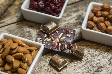 Pieces of black, chocolate with cranberry , nuts and almond  on wood background