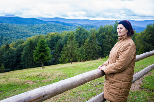 Happy elderly woman standing on top of the hill and enjoying mountain view, harmony concept