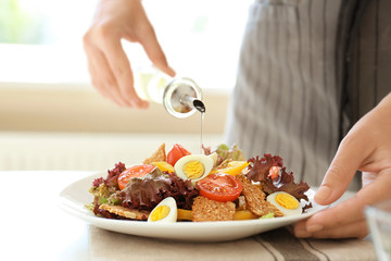Woman dressing fresh vegetable salad on white plate