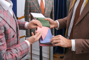 Tailor with client in atelier. Choosing fabric for custom made suit
