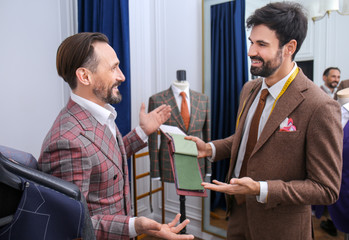 Tailor with client in atelier. Choosing fabric for custom made suit