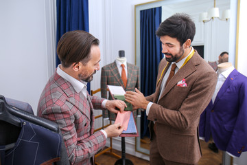 Obraz premium Tailor with client in atelier. Choosing fabric for custom made suit