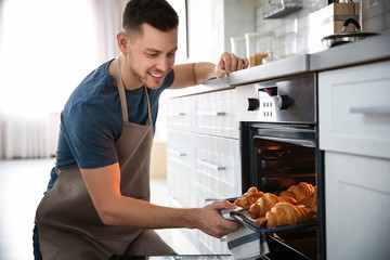 Man taking baking tray with delicious croissants out of electric oven in kitchen