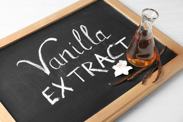 Chalkboard with glass bottle of vanilla extract on table