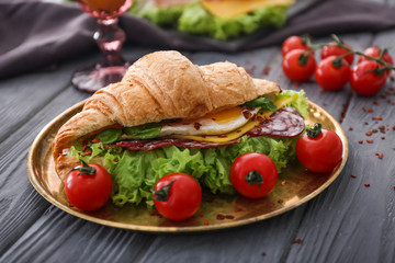 Plate with tasty croissant sandwich on table