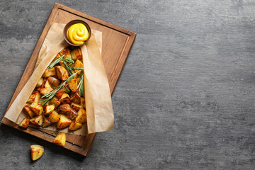 Wooden board with tasty potato wedges and mustard on table