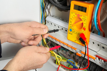 Young electrician measuring voltage in distribution board, closeup