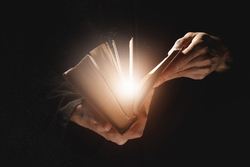 Priest with old Bible on black background, closeup