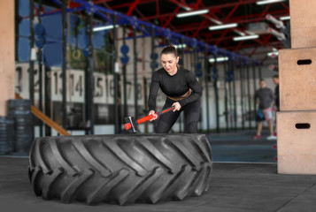 Fototapeta premium Young muscular woman hitting heavy tire with hammer in gym